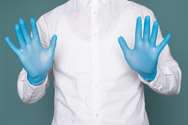 Kostenloses Foto ein junger mann der vorderansicht, der seine hände mit blauen handschuhen auf dem blauen raum zeigt