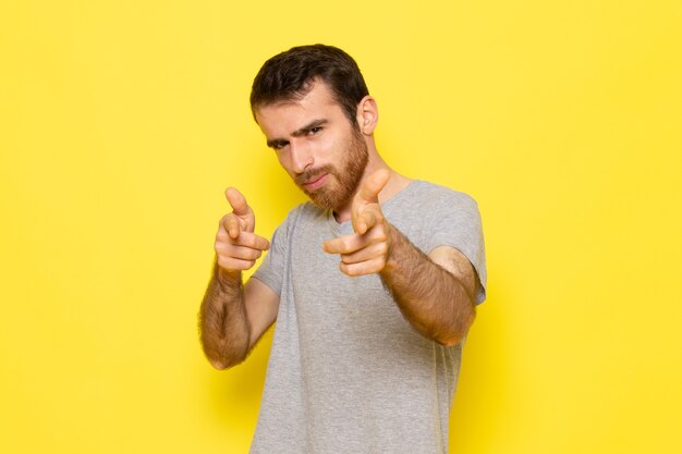 Ein junger Mann der Vorderansicht im grauen T-Shirt, das auf dem Farbmodell der gelben Wandmannausdrucksemotion aufwirft