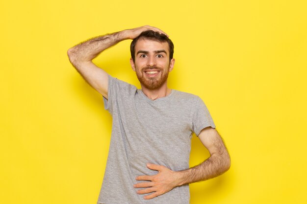 Ein junger Mann der Vorderansicht im grauen T-Shirt, das lächelnd und auf der gelben Wandmann-Farbmodell-Emotionskleidung posiert