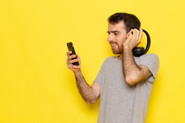 Ein junger Mann der Vorderansicht im grauen T-Shirt, das Musik auf dem Farbmodell der gelben Wandmannausdrucksemotion hört