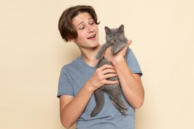 Ein junger Mann der Vorderansicht im grauen T-Shirt, das niedliches graues Kätzchen hält