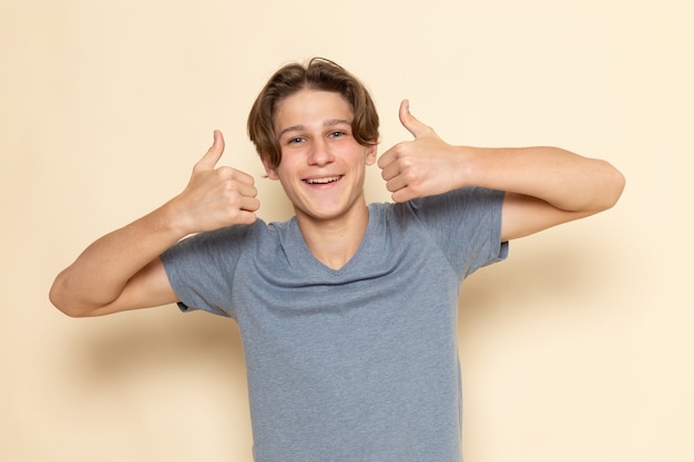 Kostenloses Foto ein junger mann der vorderansicht im grauen t-shirt, das wie zeichen mit lächeln zeigt