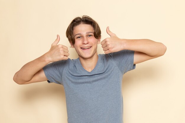 Ein junger Mann der Vorderansicht im grauen T-Shirt, das wie Zeichen mit Lächeln zeigt