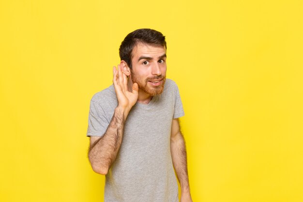 Ein junger Mann der Vorderansicht im grauen T-Shirt, der versucht, auf der gelben Wandmann-Farbmodell-Emotionskleidung zu hören