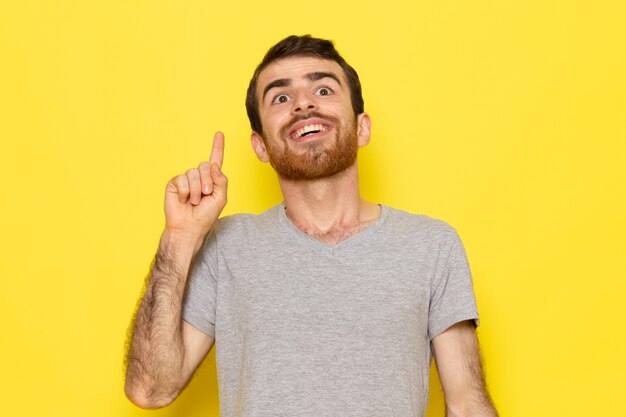 Ein junger Mann der Vorderansicht im grauen T-Shirt mit lustigem Ausdruck auf dem gelben Wandmannausdruck-Emotionsfarbmodell