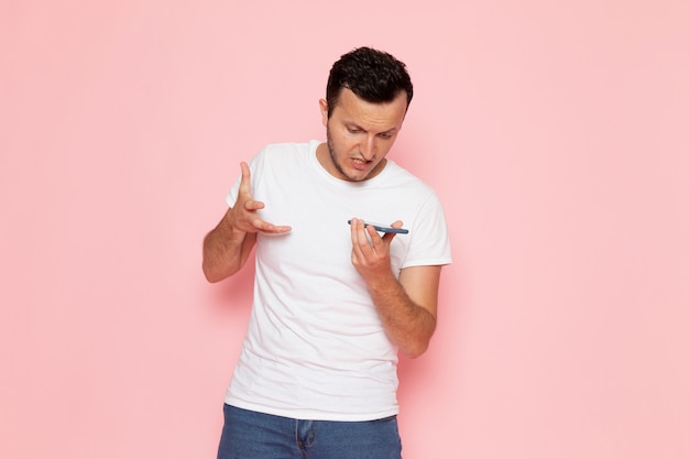 Ein junger Mann der Vorderansicht im weißen T-Shirt, das am Telefon auf der Farbemotionshaltung des rosa Schreibtischmannes spricht