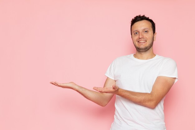 Ein junger Mann der Vorderansicht im weißen T-Shirt, das auf der rosa Wandmann-Farbhaltung aufwirft und lächelt