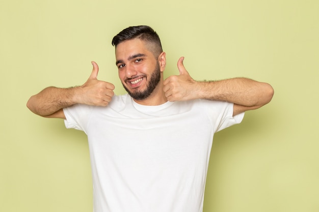 Ein junger mann der vorderansicht im weißen t-shirt, das wie zeichen mit lächeln zeigt