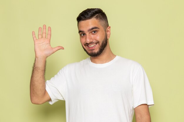 Ein junger Mann der Vorderansicht im weißen T-Shirt grüßt und lächelt