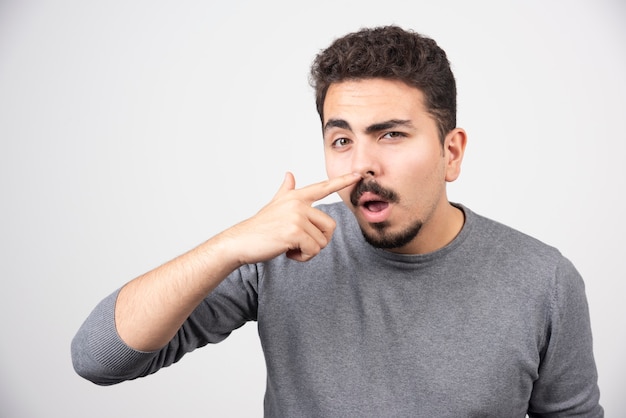 Ein junger Mann kratzte sich mit der Nase über einer weißen Wand.