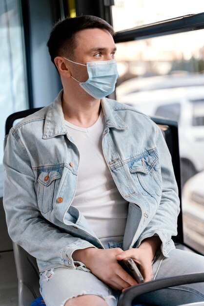 Ein junger Mann mit einer chirurgischen Maske, der mit dem Stadtbus fährt