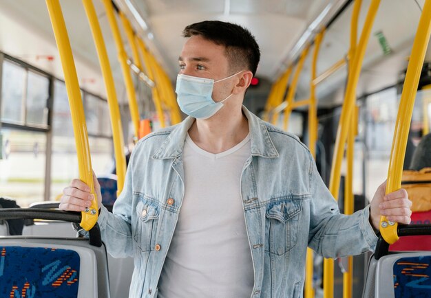 Ein junger Mann mit einer chirurgischen Maske, der mit dem Stadtbus fährt