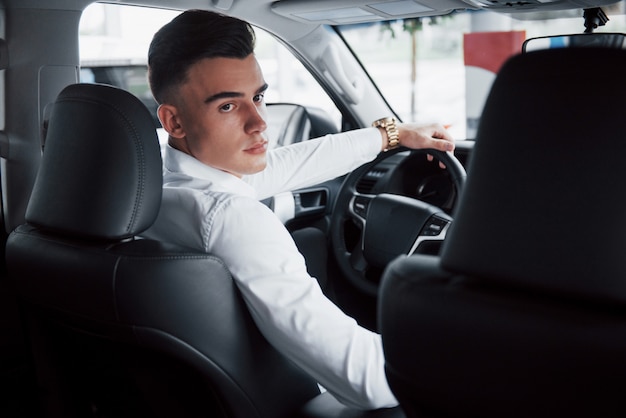 Ein junger Mann sitzt in einem neu gekauften Auto am Steuer, ein erfolgreicher Kauf.