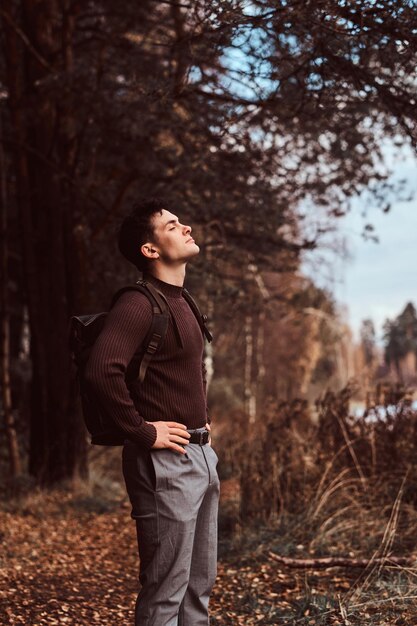 Ein junger Wanderer mit einem Rucksack, der einen Pullover trägt und einen Spaziergang im Herbstwald genießt.