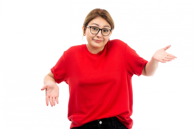 Ein junges attraktives Mädchen der Vorderansicht im roten T-Shirt, das schwarze Jeans in der Sonnenbrille trägt, die auf dem Weiß aufwirft