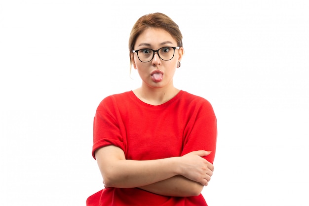 Ein junges attraktives mädchen der vorderansicht im roten t-shirt, das schwarze jeans in der sonnenbrille trägt, die lustige gesichter auf dem weiß machen