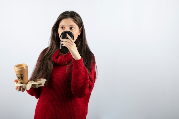 Ein junges frauenmodell im roten pullover mit zwei tassen kaffee