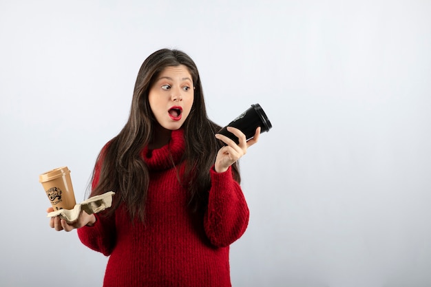 Ein junges Frauenmodell im roten Pullover mit zwei Tassen Kaffee