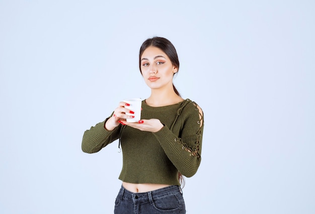 Ein junges hübsches Frauenmodell, das einen Plastikbecher mit heißem Getränk hält.