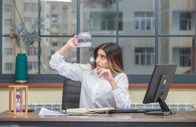 Ein junges Mädchen, das hinter dem Schreibtisch sitzt und ihre leere Teetasse betrachtet Hochwertiges Foto