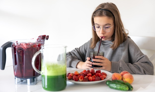 Ein junges Mädchen trinkt einen Beeren-Smoothie, während es in der Küche sitzt