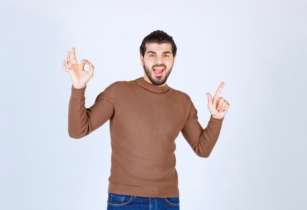 Ein junges männliches Modell in der braunen Strickjacke, die über der weißen Wand steht. Foto in hoher Qualität