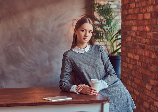 Ein junges, schlankes, sexy Mädchen in einem grauen Kleid hält eine Tasse Kaffee