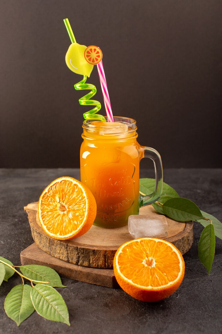 Kostenlose Foto ein kalter cocktail der vorderansicht, der innerhalb der glasdose mit buntem strohhalm mit eiswürfelorangen und grünen blättern gefärbt wird, isoliert auf dem hölzernen schreibtisch und dunkel