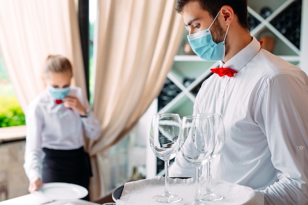 Ein kellner in einer medizinischen schutzmaske bedient einen tisch im restaurant. mitarbeiter eines restaurants oder hotels in schutzmasken. das ende der quarantäne.