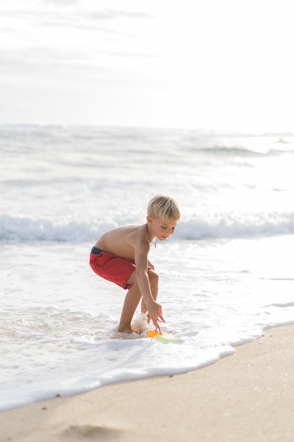 Ein Kind am Strand spielt in den Wellen des Ozeans. Junge auf dem Ozean, glückliche Kindheit. tropisches leben.