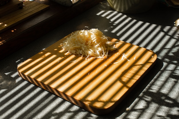 Ein kleiner Haufen geriebener Frischkäse liegt auf einem Holzbrett in der Küche