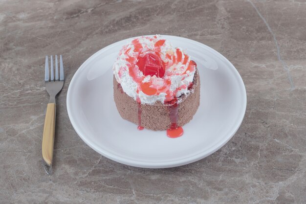 Ein kleiner Kuchen mit Sahne und Erdbeersirup auf einem Teller auf Marmor