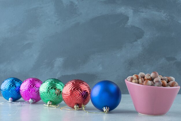 Ein kleiner rosa Teller voller Nüsse mit Weihnachtskugeln auf Marmorhintergrund. Hochwertiges Foto