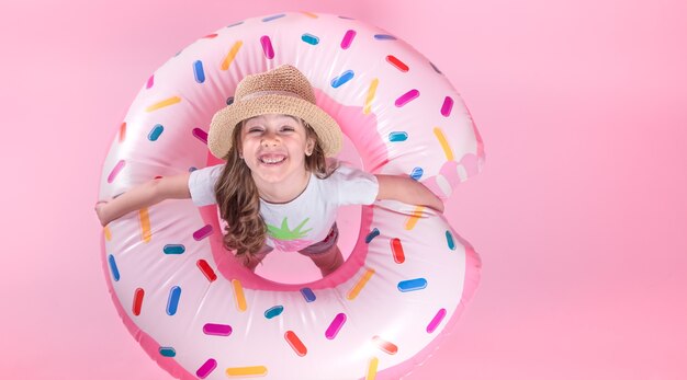 Ein kleines Kindermädchen in Freizeitkleidung, das auf einem aufblasbaren Donutkreis liegt. Rosa Hintergrund. Draufsicht. Sommerkonzept.