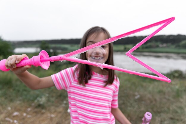 Ein kleines lustiges Mädchen bläst im Sommer Seifenblasen auf einem Feld, Sommeraktivitäten im Freien.