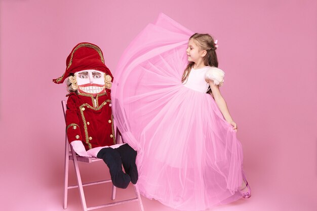 Ein kleines Mädchen als Schönheitsballerina am rosa langen Kleid mit Nussknacker am rosa Studio