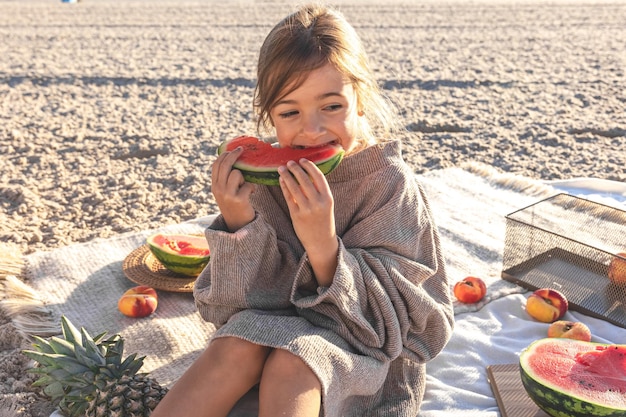 Ein kleines Mädchen an einem Sandstrand isst eine Wassermelone