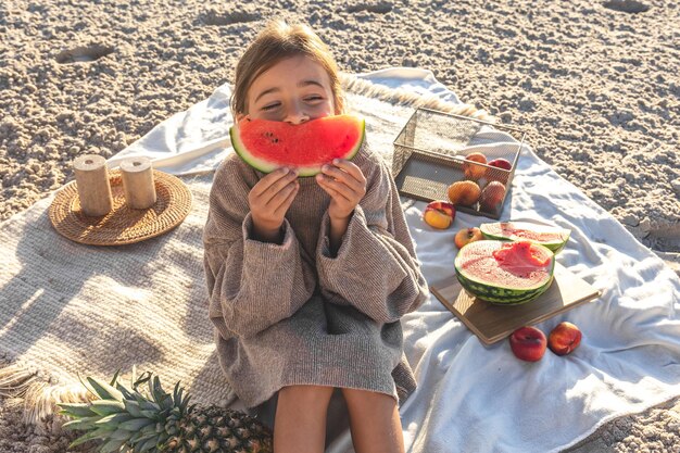 Ein kleines Mädchen an einem Sandstrand isst eine Wassermelone