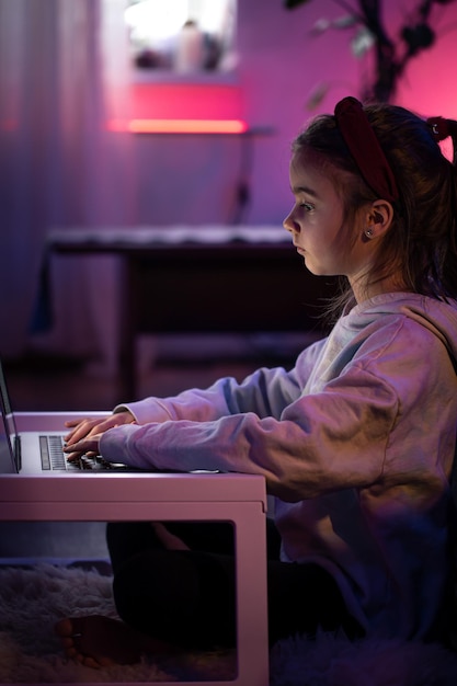 Ein kleines mädchen benutzt einen laptop, während es in einem raum mit neonbeleuchtung sitzt Kostenlose Fotos