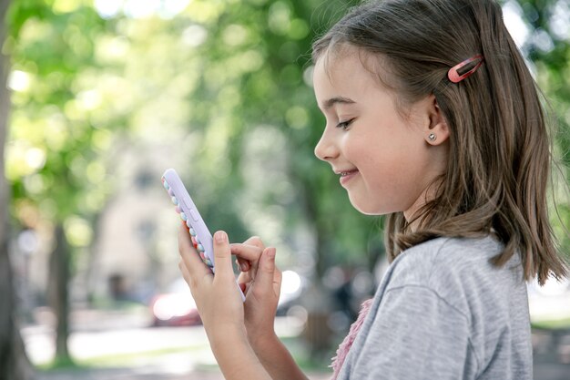 Ein kleines Mädchen hält in der Hand ein Telefon in einer Hülle mit Pickeln, ein trendiges Anti-Stress-Spielzeug.