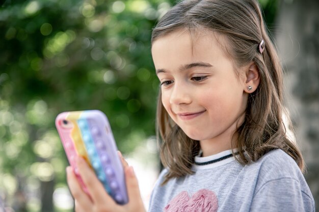 Ein kleines Mädchen hält in der Hand ein Telefon in einer Hülle mit Pickeln, ein trendiges Anti-Stress-Spielzeug.