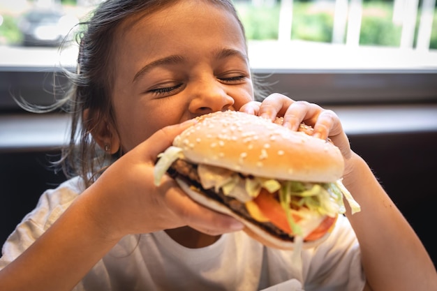 Ein kleines Mädchen isst eine appetitliche Burger-Nahaufnahme