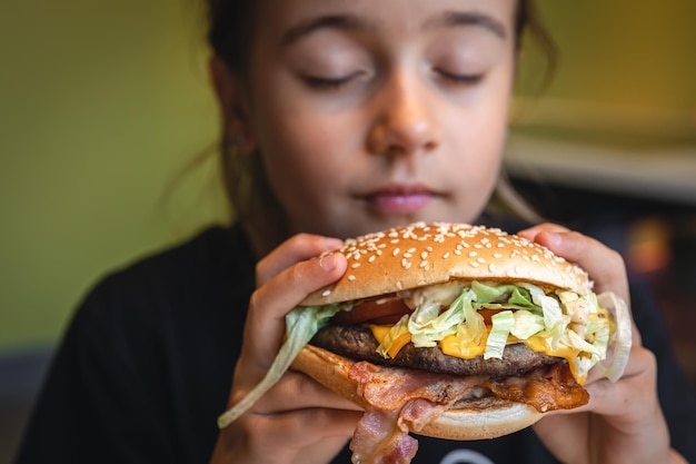 Ein kleines Mädchen isst eine appetitliche Burger-Nahaufnahme