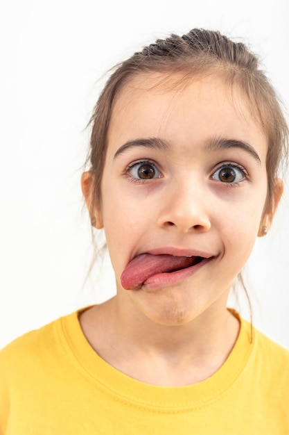 Ein kleines Mädchen macht Grimassen mit ihrer Zunge, die auf einem weißen Hintergrund hängt