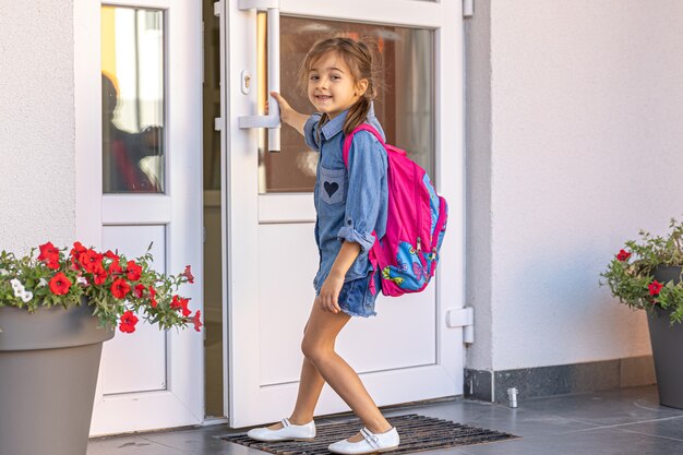 Ein kleines Mädchen mit Rucksack, ein Schulmädchen öffnet die Türen der Schule.