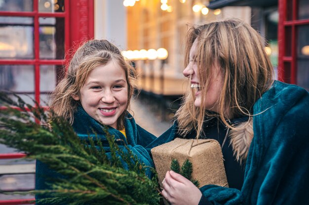 Ein kleines Mädchen und eine junge Frau mit Thujazweigen und einem Geschenk unter einem Plaid