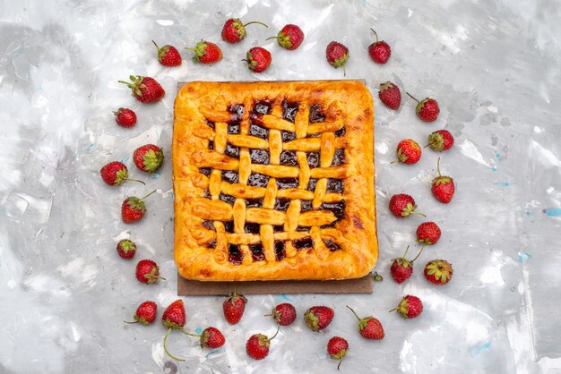 Ein köstlicher Erdbeerkuchen der Draufsicht mit Erdbeergelee innen zusammen mit frischen Erdbeeren auf dem grauen Schreibtischkuchen-Desserttee