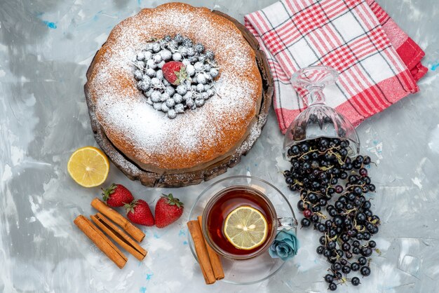 Ein köstlicher und runder Obstkuchen von oben mit frischem Blau, Beeren und Tee auf hellem Kuchenkeks süßem Zucker