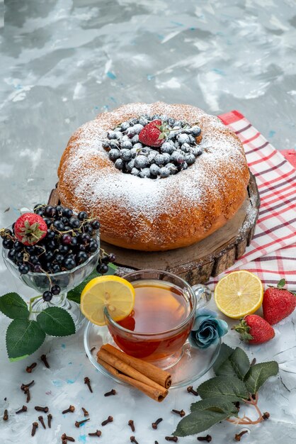 Ein köstlicher und runder Obstkuchen von vorne mit frischem Blau, Beeren und einer Tasse Tee auf hellem, süßem Zucker aus Kuchen