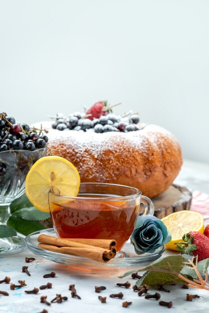 Ein köstlicher und runder Obstkuchen von vorne mit frischem Blau, Beeren und einer Tasse Tee auf hellem, süßem Zucker aus Kuchen